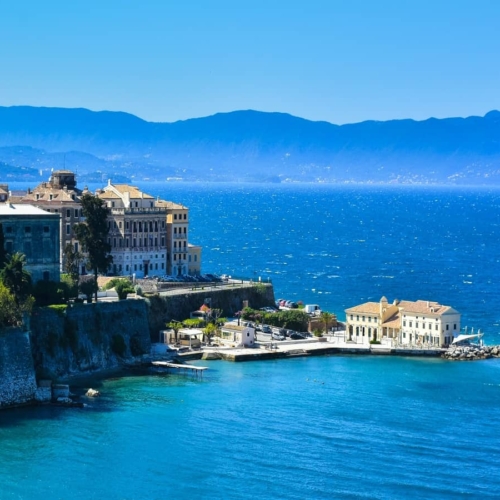 aerial view of buildings on corfu island surrounded by water with mountain range in distance