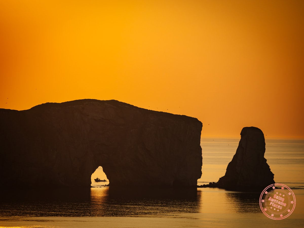 closeup of perce rock with boat passing through the arch at sunrise