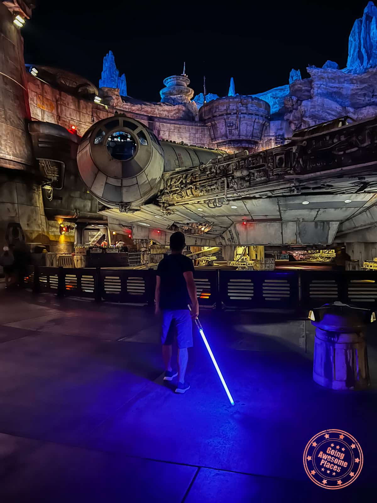 savi's workshop blue lightsaber glowing in front of millennium falcon in galaxy's edge