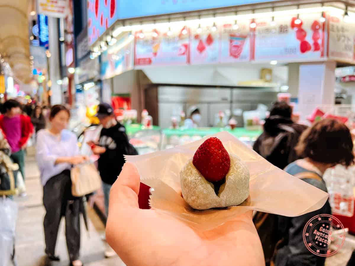 holding a strawbery mochi in front of strawberry mania in osaka
